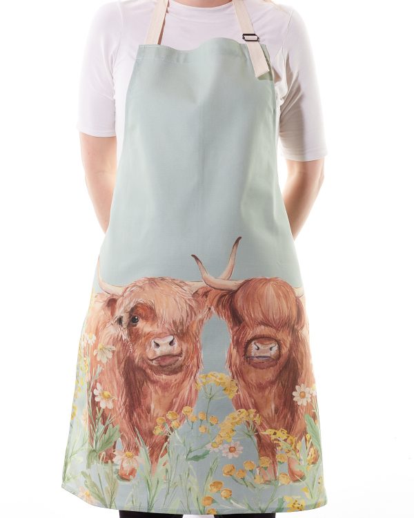Highland Cow Apron. Made from a durable cotton–linen blend, its soft pastel-blue background showcases two endearing Highland cow faces framed by daisies and buttercups
