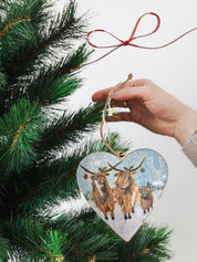 Tin heart-shaped hanging Christmas decoration depicting three adorable Highland cows adorned with Christmas baubles, holly, and festive details.
