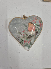 Delicate tin heart Christmas decoration illustrating a cute robin perched on a holly bush with a wintry background, evoking seasonal cheer.