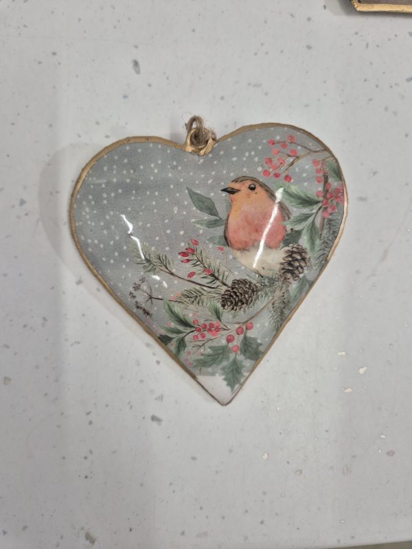 Delicate tin heart Christmas decoration illustrating a cute robin perched on a holly bush with a wintry background, evoking seasonal cheer.